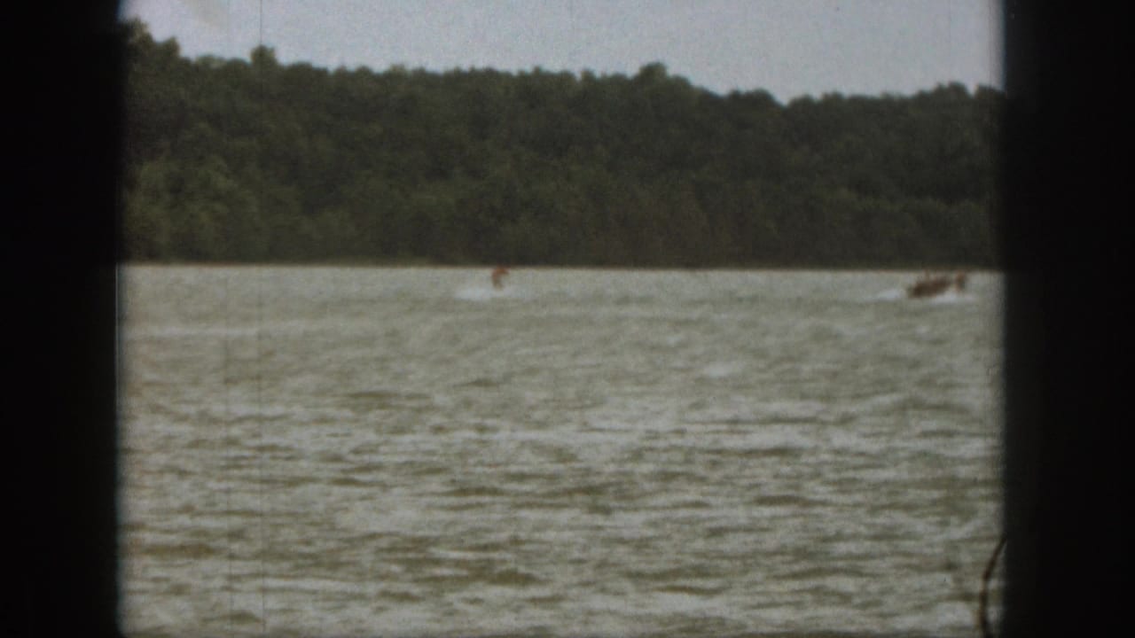 1961 Michigan home-movie frame with a distant water skier crossing choppy lake water near a towing motorboat.
