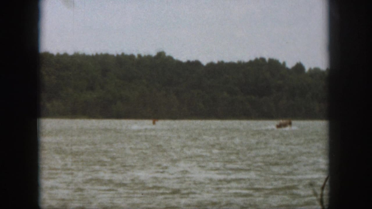 End frame of a 1961 Michigan lake scene, with the skier and boat distant against forest and rippled water.