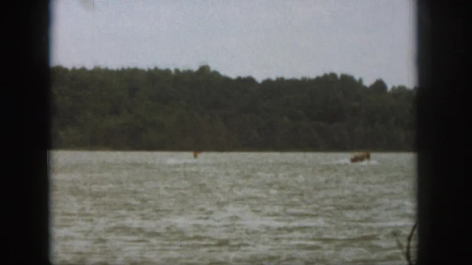 End frame of a 1961 Michigan lake scene, with the skier and boat distant against forest and rippled water.