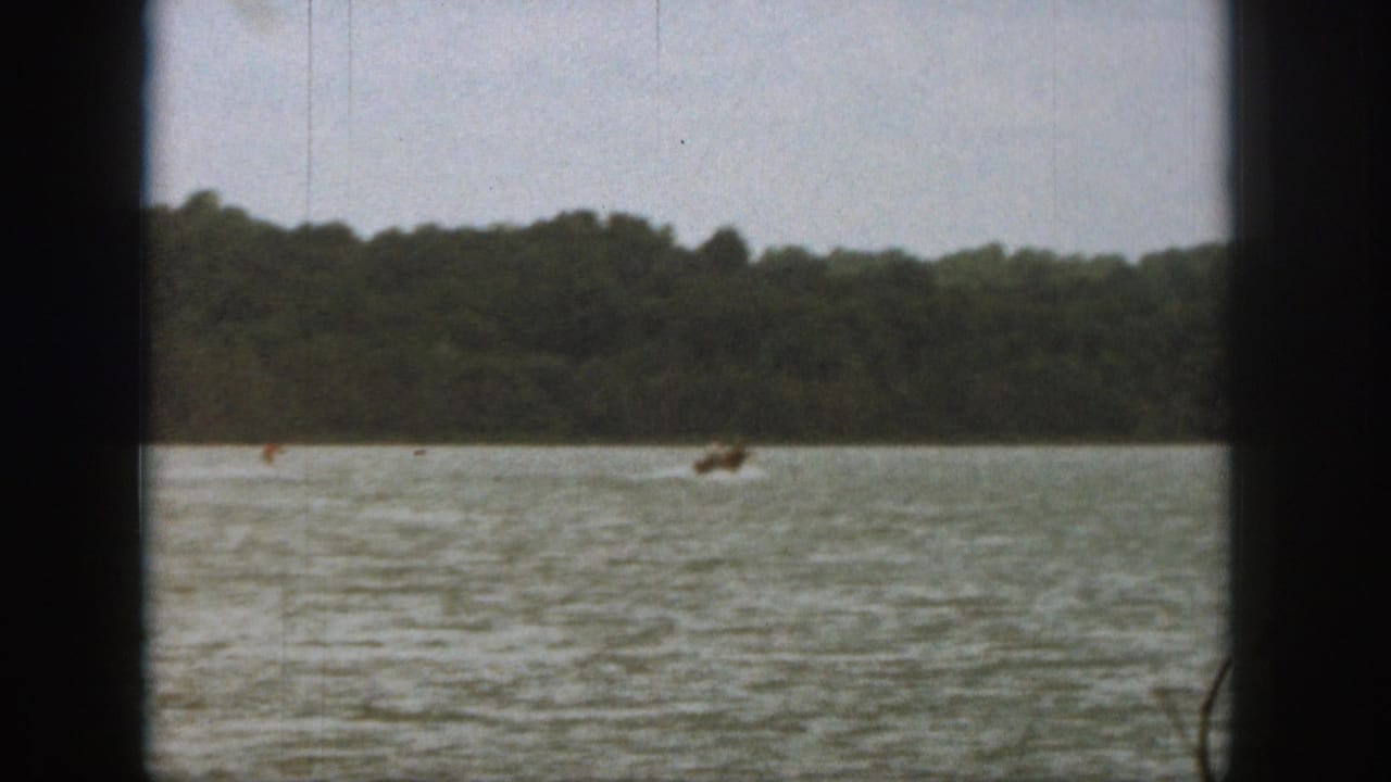 Distant water skier on a lake with wooded shoreline and dark film borders.