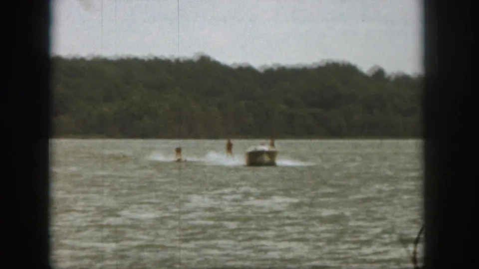 1961 Michigan lake scene with a small motorboat pulling two water skiers through choppy water.