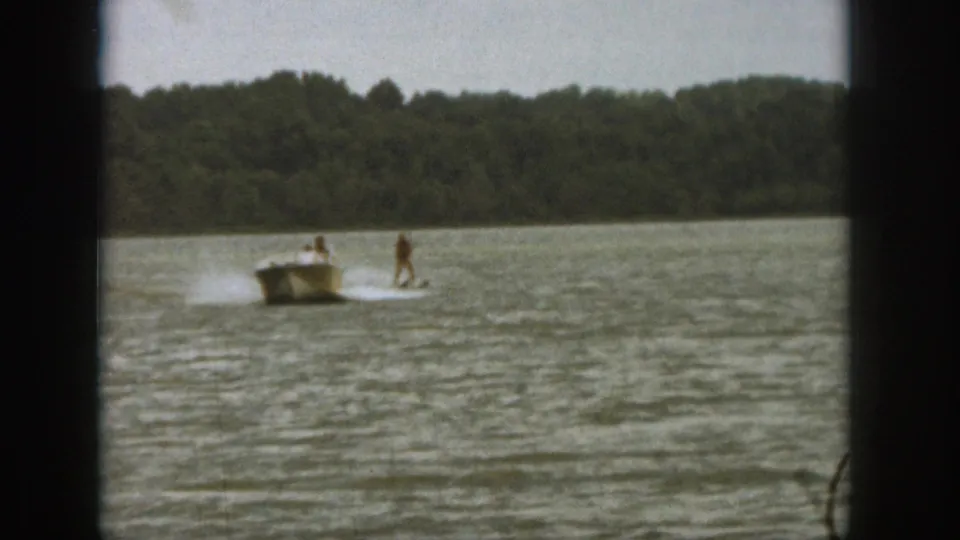 1961 Michigan lake footage shows one skier still upright behind a motorboat while another appears down in the water.