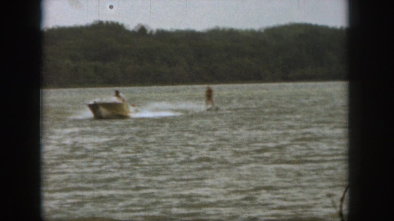 1961 Michigan 8mm frame showing a motorboat pulling a distant rider over rippled lake water, with a treeline beyond.