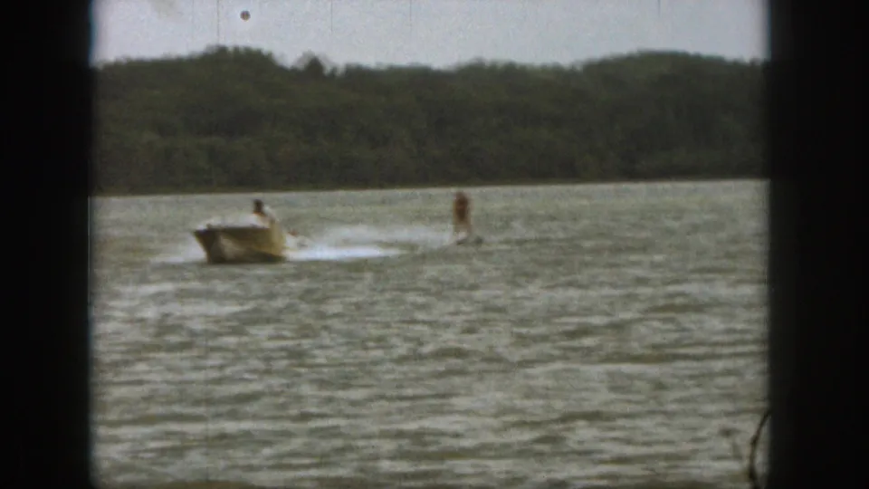 1961 Michigan 8mm frame showing a motorboat pulling a distant rider over rippled lake water, with a treeline beyond.
