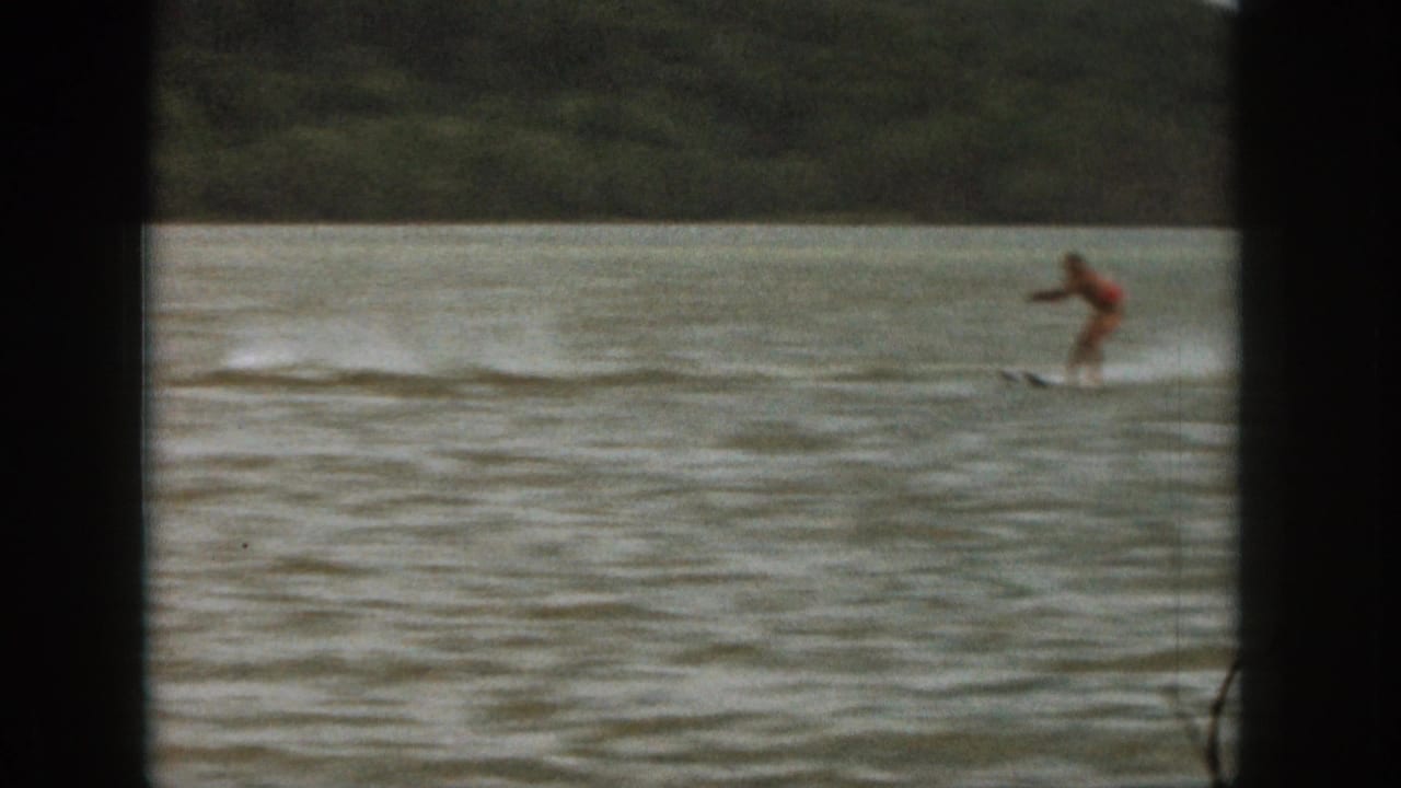 1961 Michigan 8mm frame showing a distant person in red being towed on a board across rippled lake water.