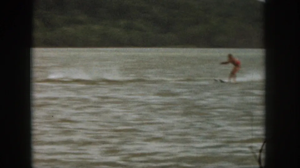 1961 Michigan 8mm frame showing a distant person in red being towed on a board across rippled lake water.