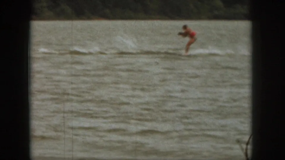 1961 Michigan lake frame with a distant red-clad rider leaning forward while being towed over choppy water.