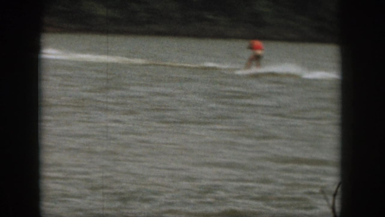 1961 Michigan 8mm frame with a small distant rider in red crossing a broad white wake on lake water.