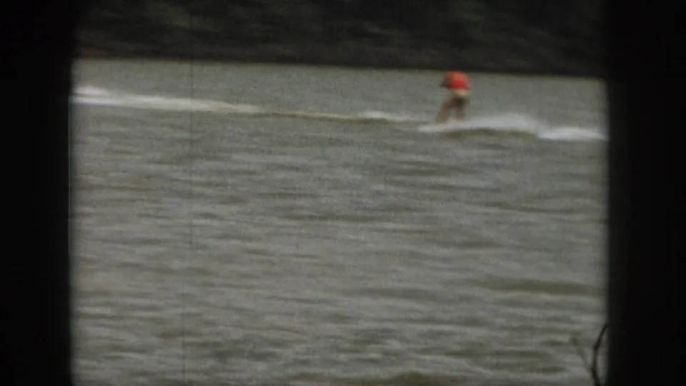 1961 Michigan 8mm frame with a small distant rider in red crossing a broad white wake on lake water.