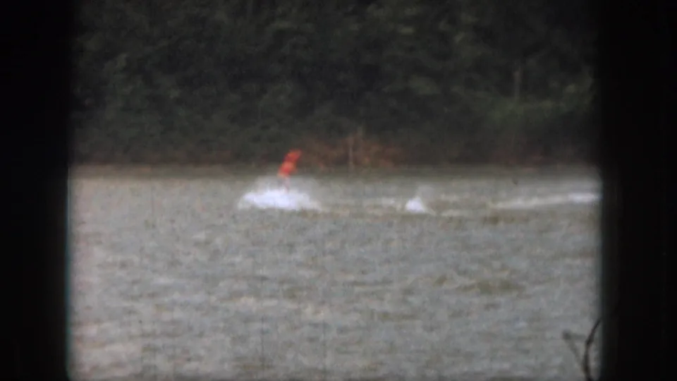 The skier appears low over the water while crossing a Michigan lake in grainy 1961 home-movie footage.
