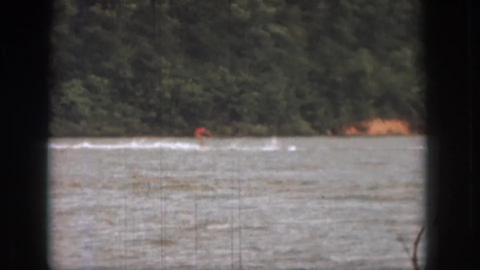 The water skier remains small in frame, moving fast across a Michigan lake in this 1961 8mm home-movie view.