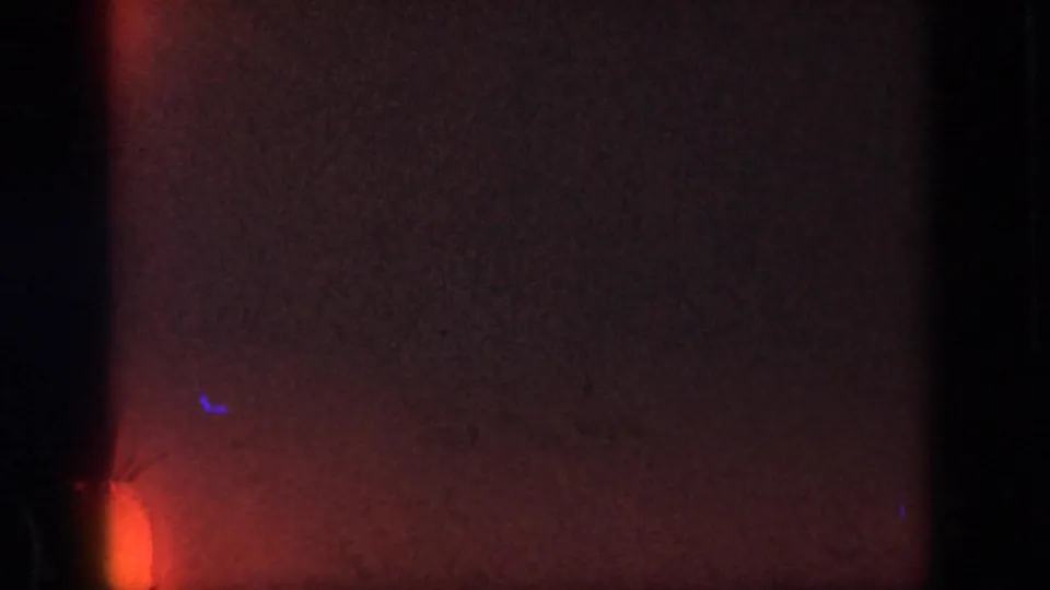 Red-tinted 8mm frame with heavy grain, a warm light leak at the lower left, and dark vertical film borders before the action appears.