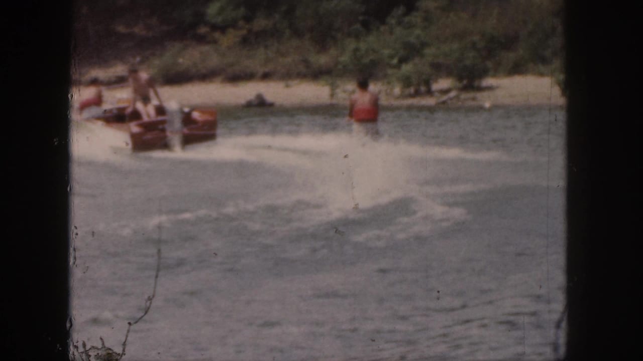 Motorboat passengers look toward a water skier crossing the lake wake.