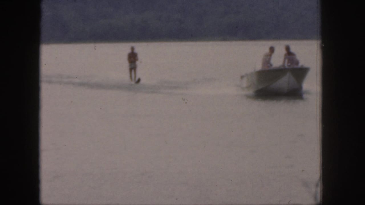 Water skier trails behind a small motorboat on a calm lake.