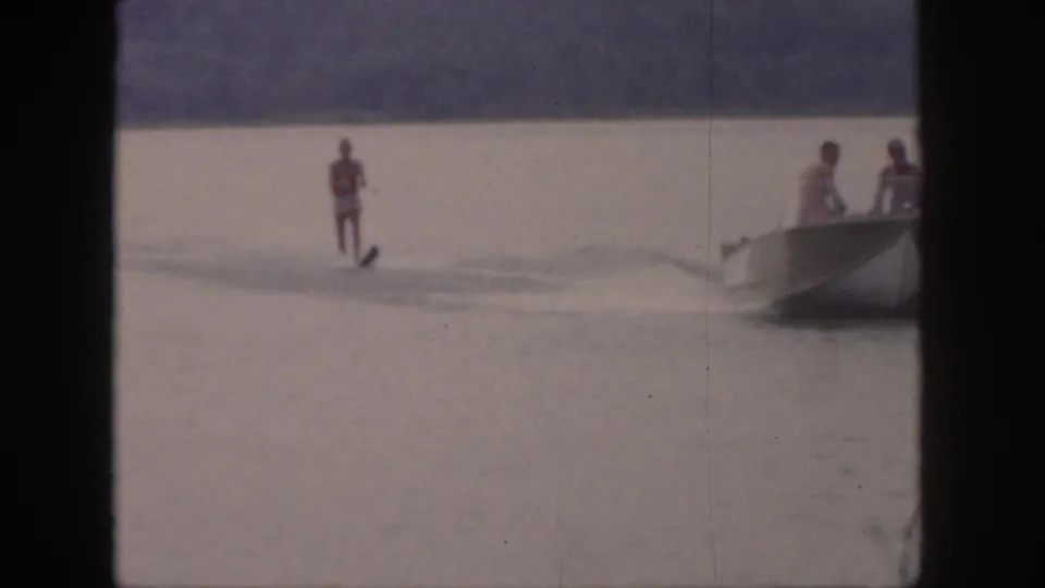 1961 Michigan 8mm frame showing a red-vested water skier behind a motorboat on a wooded lake.
