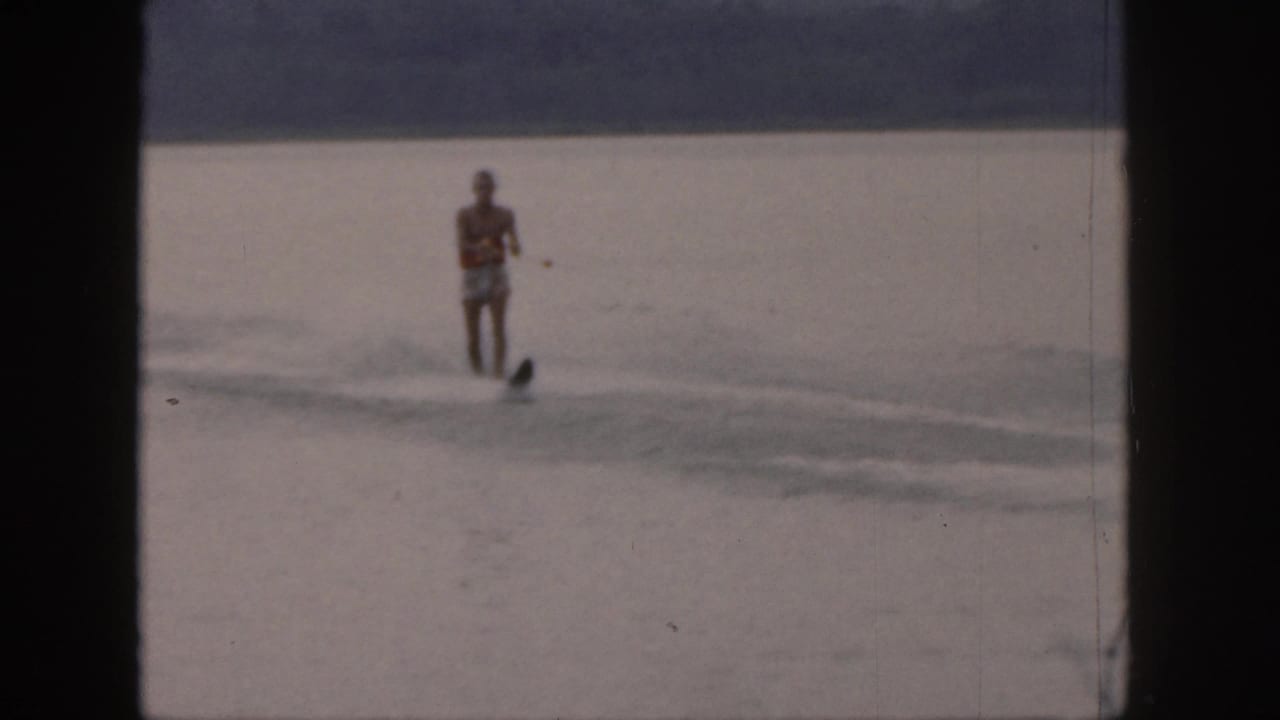 Distant man water skiing on a calm lake with spray around the ski.
