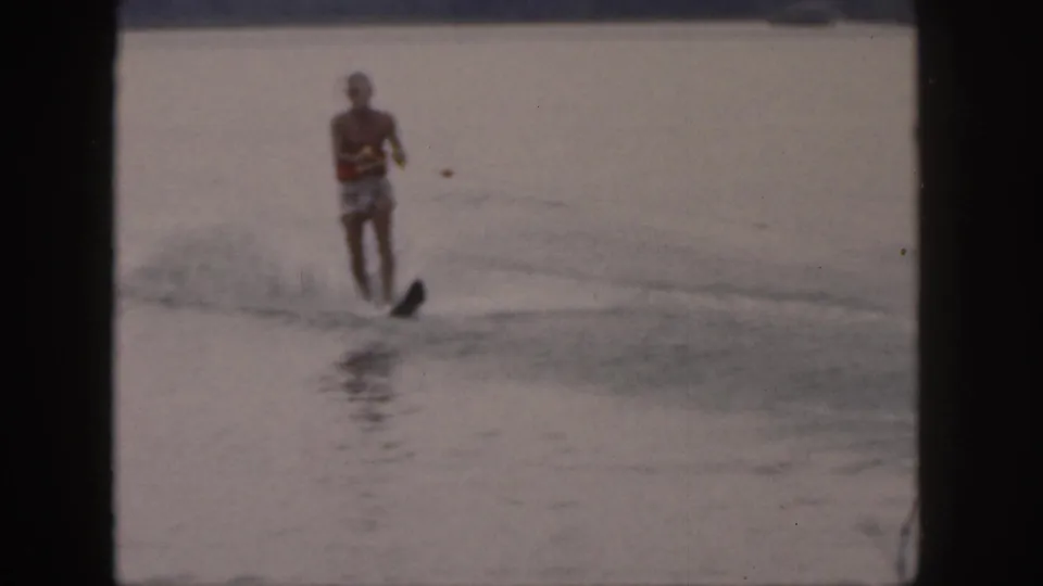 A shirtless man in patterned trunks water skis toward the camera on a Michigan lake, holding a tow rope.