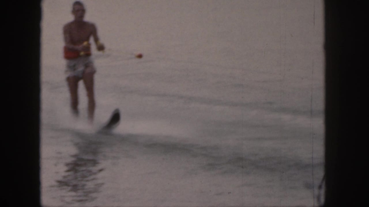 The skier passes nearer the camera, with the single ski and spray more visible in the 8mm lake footage.