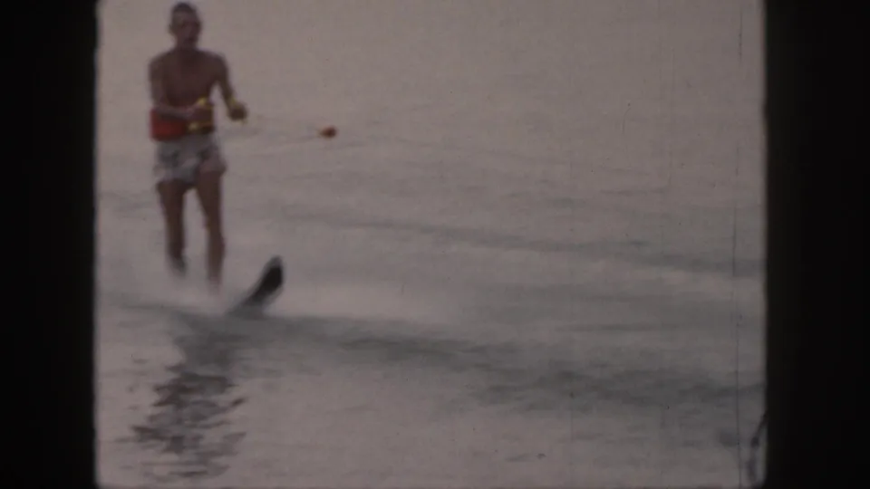 The skier passes nearer the camera, with the single ski and spray more visible in the 8mm lake footage.