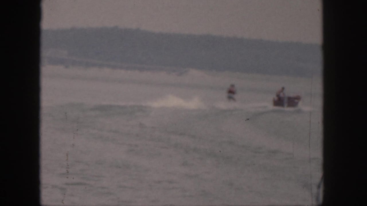 1961 Michigan 8mm frame with a distant waterskier being towed by a small motorboat across a calm lake.