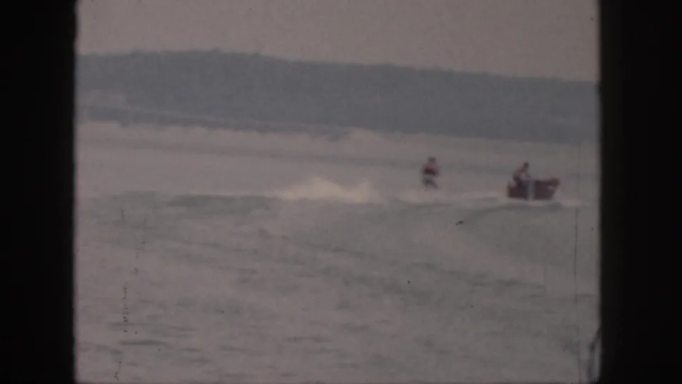 1961 Michigan 8mm frame with a distant waterskier being towed by a small motorboat across a calm lake.