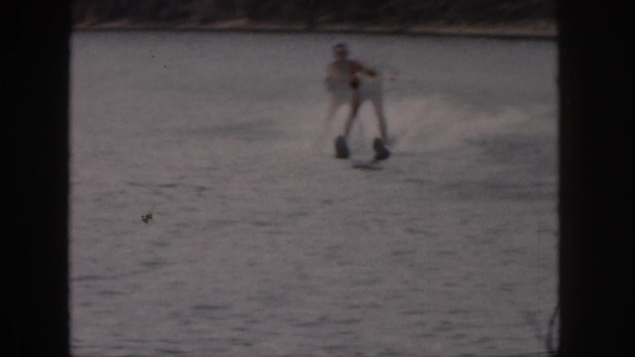 Distant man balancing on water skis on open lake water.