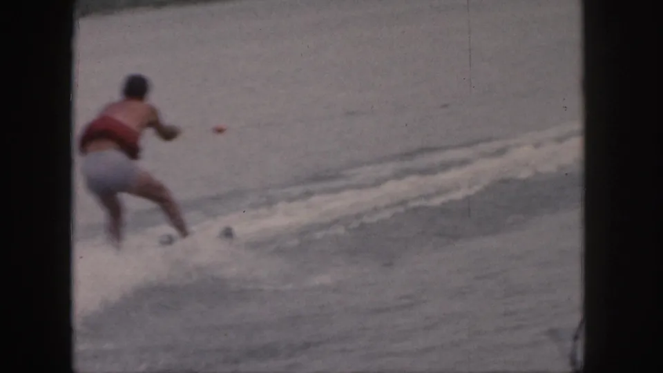1961 Michigan lake footage shows the skier moving away across the water, with wake and spray around his skis.