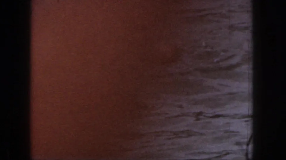 8mm frame with lake water and a reddish foreground blur, likely during the skier's fall or camera movement.