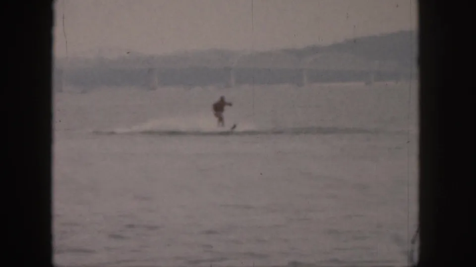 Distant water skier on a Michigan river in 1961, framed by soft-focus 8mm film borders and muted water tones.