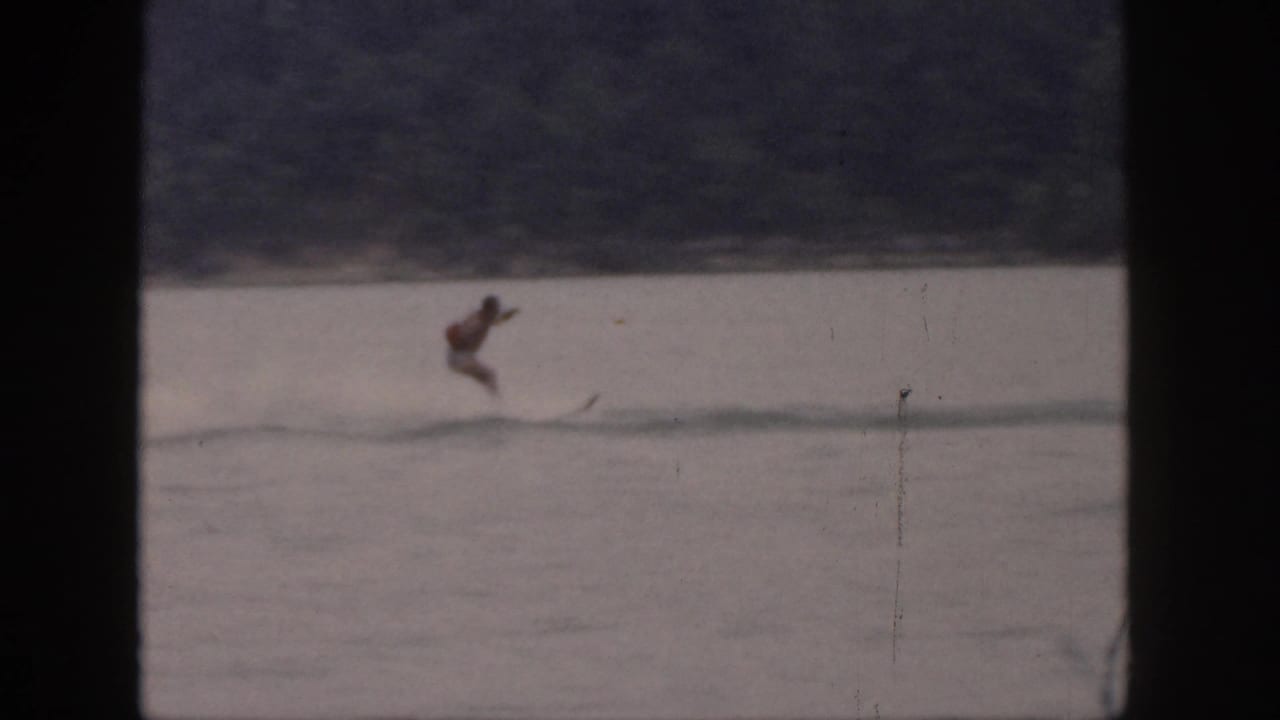 Water skier leans forward while crossing the lake near a distant shoreline.
