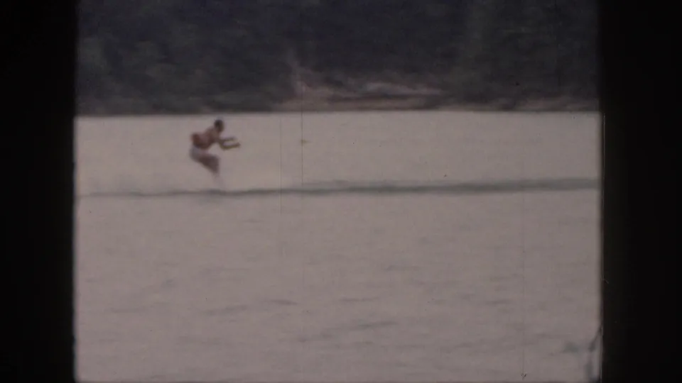 1961 Michigan home-movie still of a distant male water skier crouched low while moving across the lake.