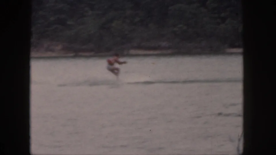 Soft 1961 Michigan 8mm frame with a male water skier moving past a tree-lined lakeshore.