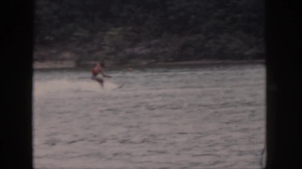 1961 Michigan lake footage shows the skier leaning low as he appears to lose balance while being towed across the water.