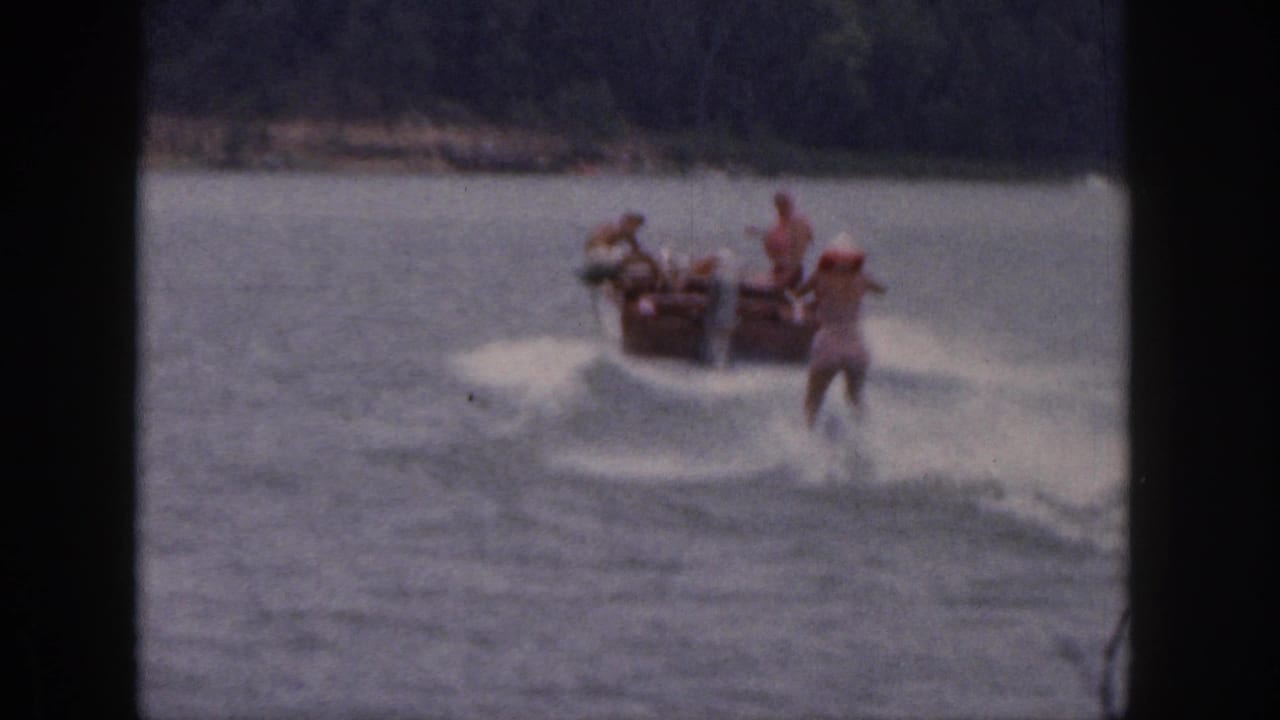 1961 Michigan 8mm home-movie frame showing a motorboat pulling a water skier in red across a calm lake.