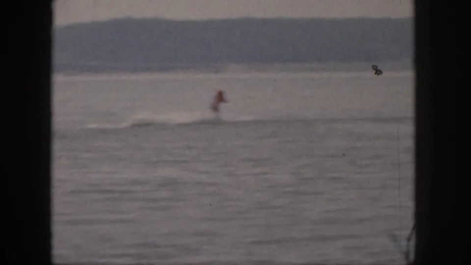 Soft 8mm frame from Michigan in 1961 showing the rider near the water surface with a low wake and wooded shoreline beyond.