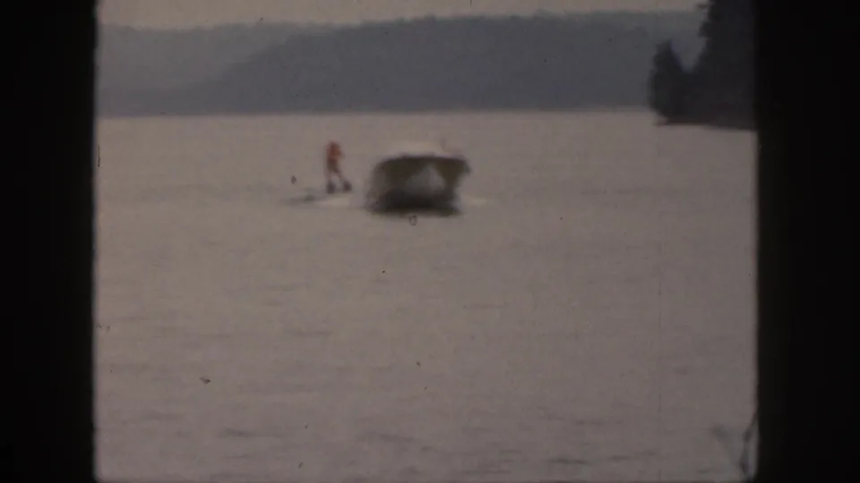 1961 Michigan home-movie frame showing a small motorboat towing a water skier across open lake water in soft focus.