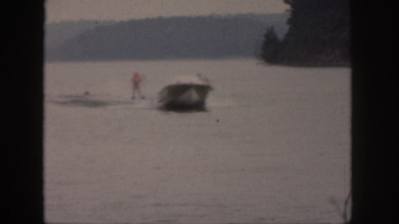 A small boat tows a distant water skier on a Michigan lake, framed by dark 8mm contact-sheet borders.