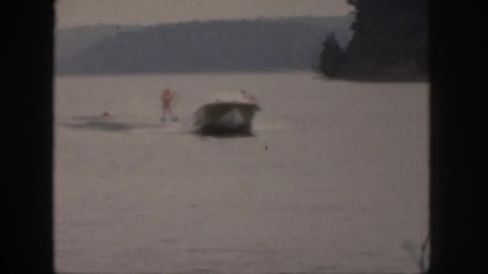 A small boat tows a distant water skier on a Michigan lake, framed by dark 8mm contact-sheet borders.