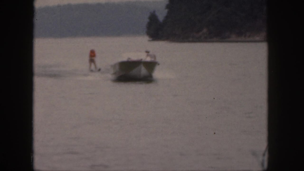 A 1961 Michigan lake scene shows a skier in an orange life vest being pulled behind a small motorboat.