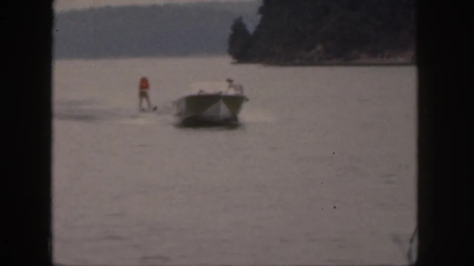 A 1961 Michigan lake scene shows a skier in an orange life vest being pulled behind a small motorboat.