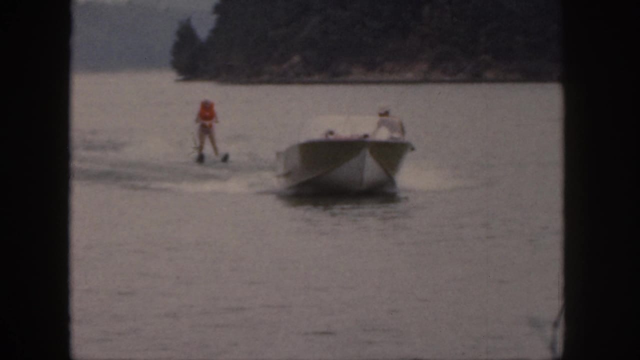 In 1961 Michigan home-movie footage, a skier in an orange life vest follows a white motorboat across a calm lake.