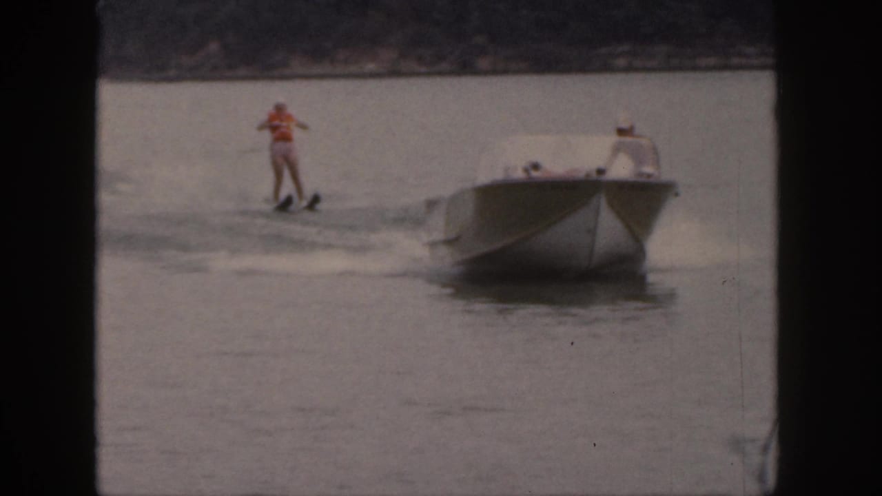 Water skier leans behind a motorboat as the boat moves across the lake.