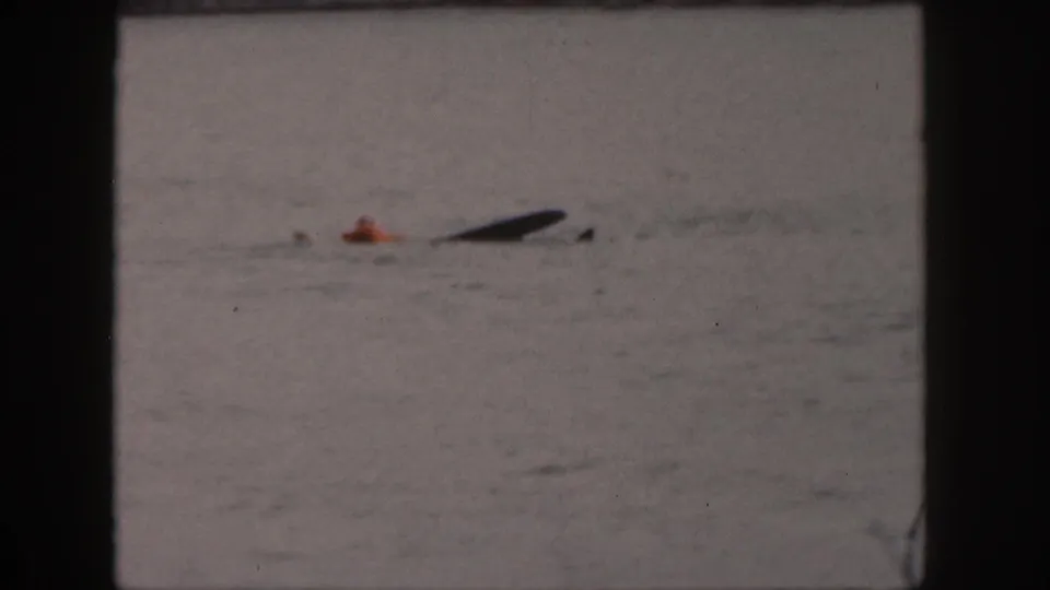 1961 Michigan 8mm frame showing a person in an orange top low in the lake water near a dark waterski or float.
