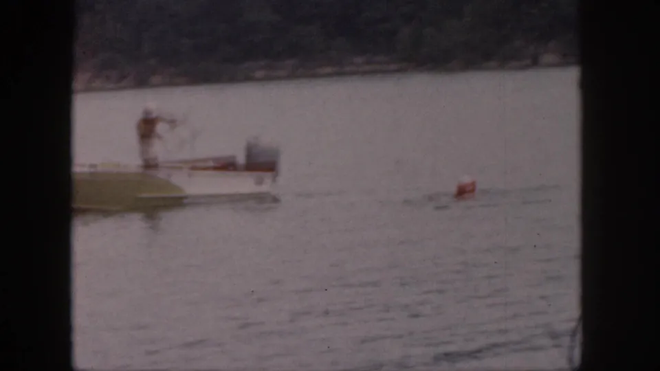 1961 Michigan home-movie still with a soft-focus motorboat scene and red buoy on rippling lake water.