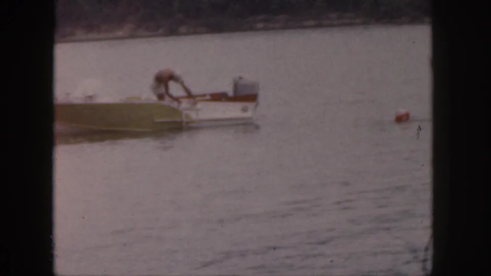 A 1961 Michigan lake scene shows a man bent over a small motorboat, with a red buoy floating to the right.