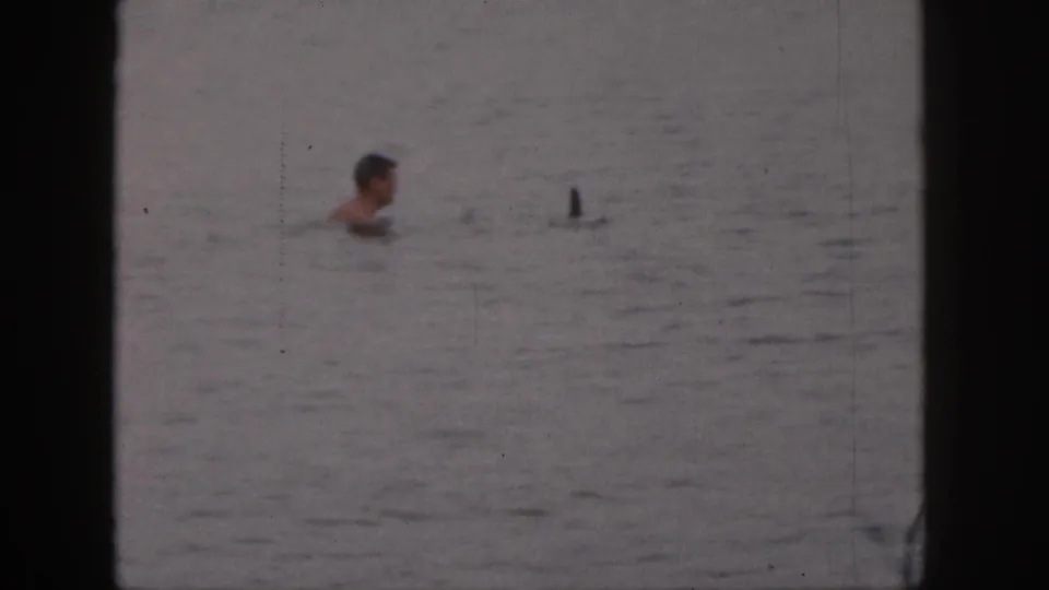 1961 Michigan 8mm frame with an adult swimmer in calm lake water and a small upright ski or board tip visible nearby.