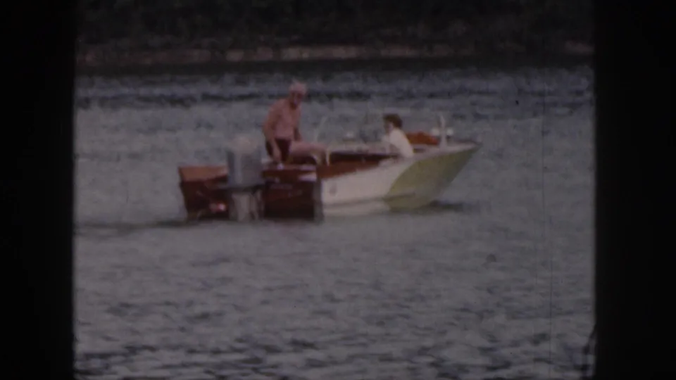1961 Michigan 8mm frame showing a small wooden motorboat on lake water with one adult at the stern and another passenger forward.