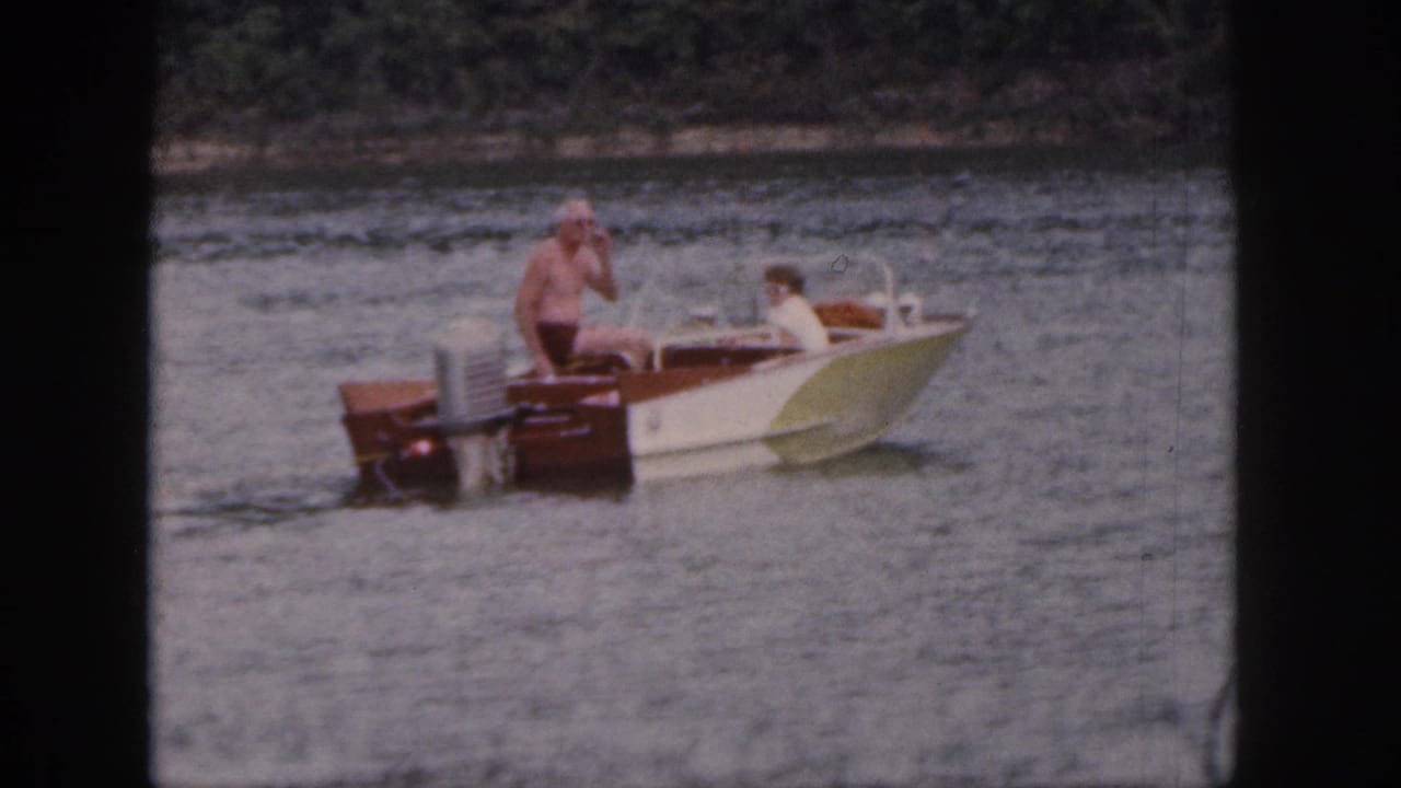 1961 Michigan home-movie frame showing a wooden motorboat on the lake with two visible people aboard.