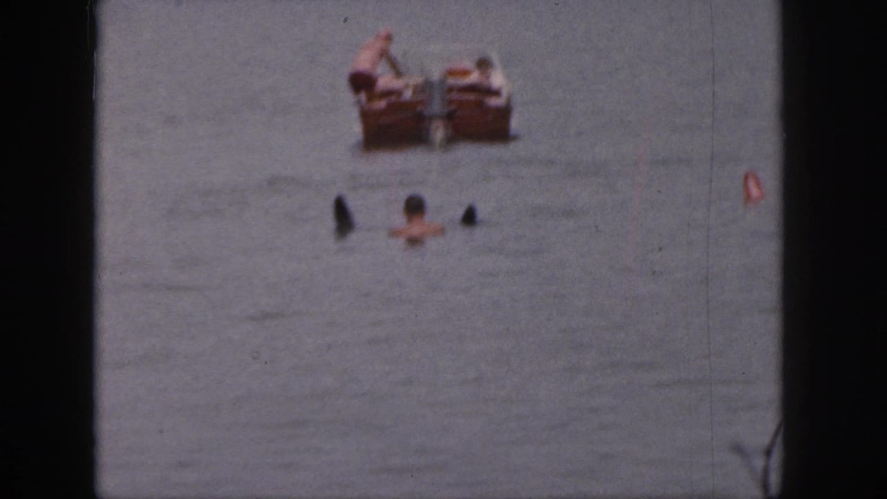 Swimmers in lake water near a distant wooden motorboat.