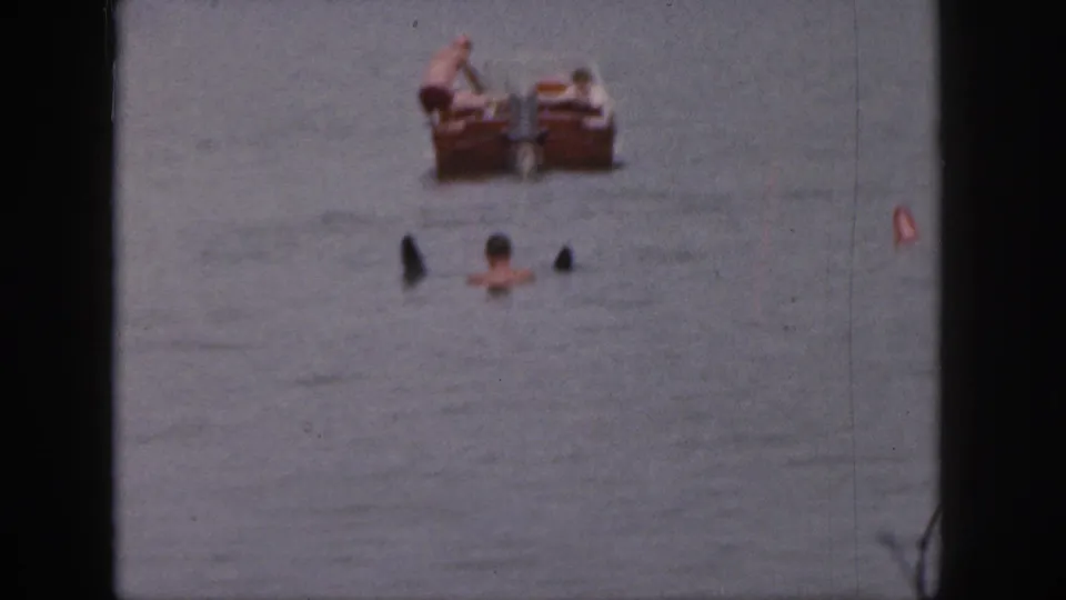 1961 Michigan lake frame with swimmers in the water and a wooden motorboat farther back.